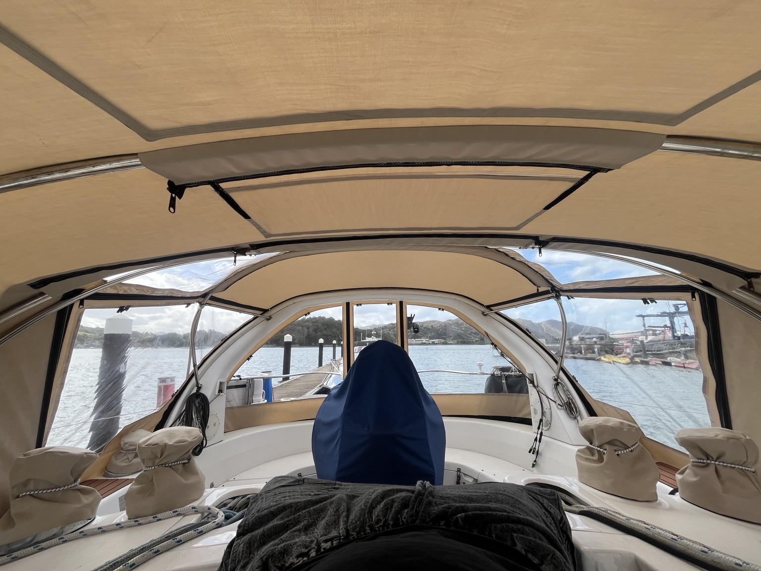 Looking aft through a beige cockpit enclosure with clear windows overlooking the marina